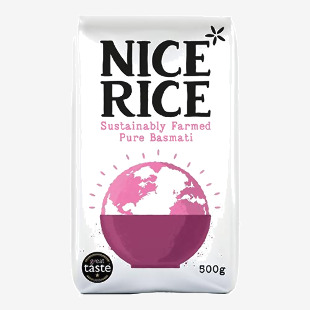 A photo shows a cardboard tray holding twelve 500g bags of Nice Rice Pure Basmati, arranged in three rows. Each bag displays the Nice Rice logo and a 'Pure Basmati' label on green-and-white packaging with a clear window revealing long white grains. The scene has soft studio light on a pale backdrop.