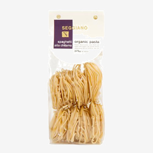 Image shows a green-and-cream Seggiano box of Organic Spaghetti alla Chitarra (375 g). A clear window reveals long, square-cut golden strands. The front features the Seggiano logo, an organic seal and Italian-style typography against a neutral grocery-shelf background. softly lit with subtle shadow.