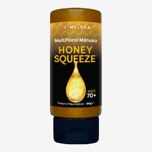 Photo shows a group of Melora Manuka Honey squeeze bottles arranged in rows. Each clear plastic bottle reveals thick golden honey. Labels feature green accents and a stylized manuka flower. White caps, honey drips from one bottle, and soft lighting highlights a glossy, viscous texture. Lush sheen now