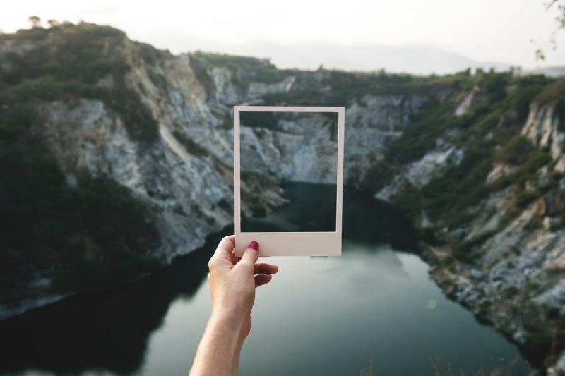 girl holding polaroid over river and hills