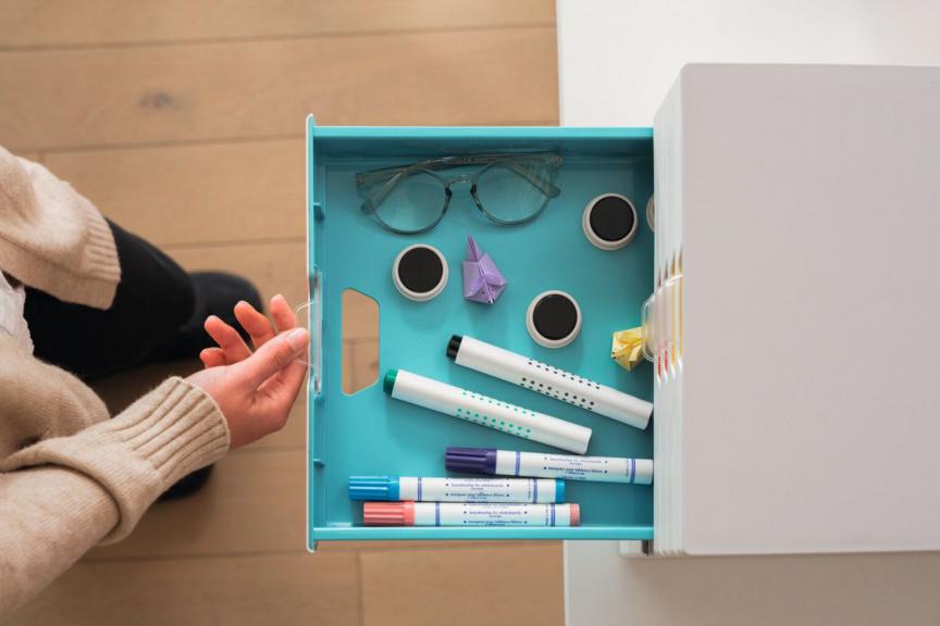 Colourful blue drawer being opened displayed with desk accessories inside. 