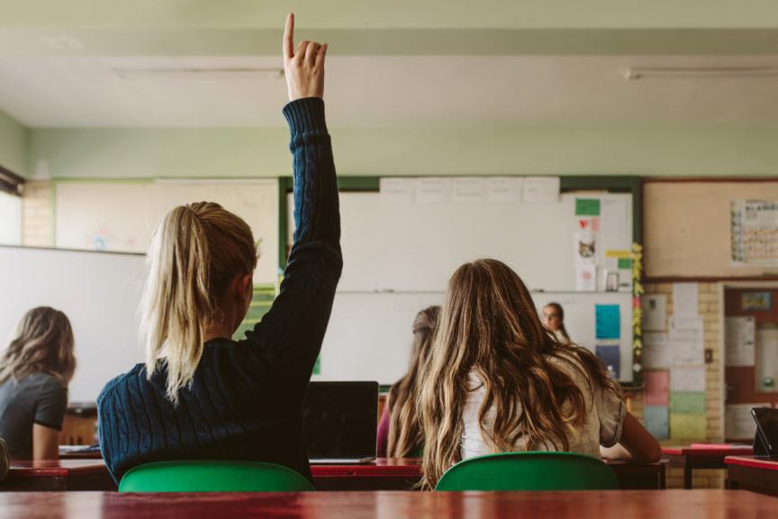 Classroom with children putting hands up. 