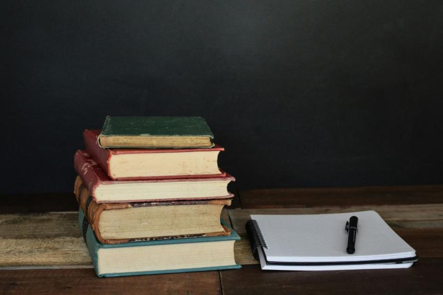 Desk with pile of books and a notepad. 